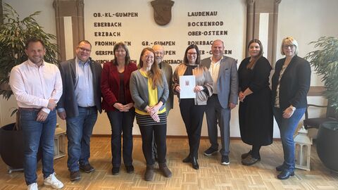 Neun Personen stehen nebeneinander in einem Raum. Eine Frau hält eine Urkunde hoch.