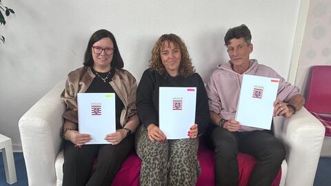 Drei Frauen sitzen auf einer Couch und halten jeweils einen Förderbescheid in den Händen.